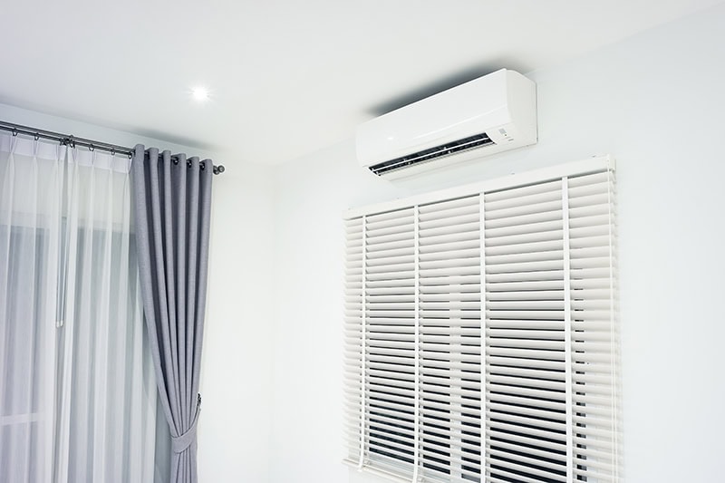 A ductless unit hanging on a wall next to some blue curtains.