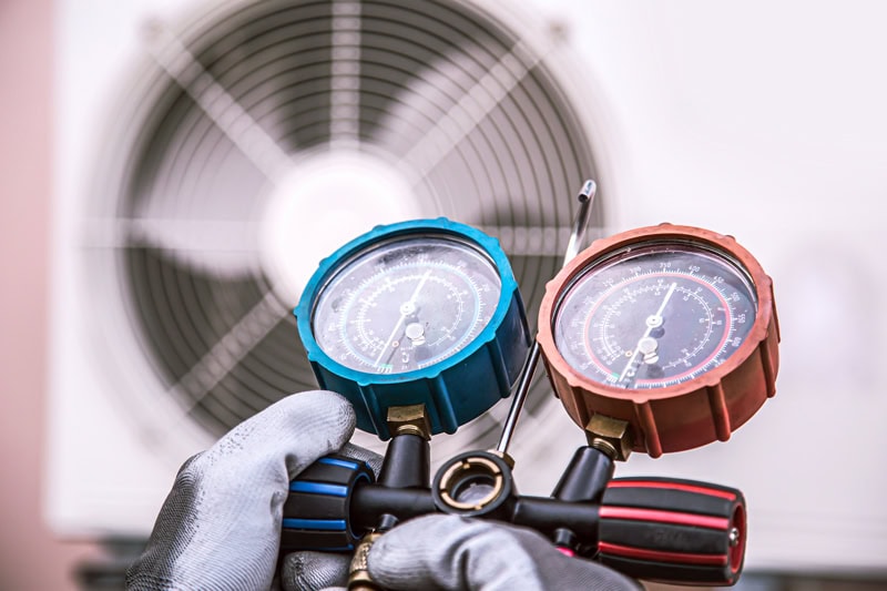 Technician checking AC refrigerant pressure with gauges in front of an outdoor condenser unit, illustrating air conditioner performance issues in extreme Texas heat.