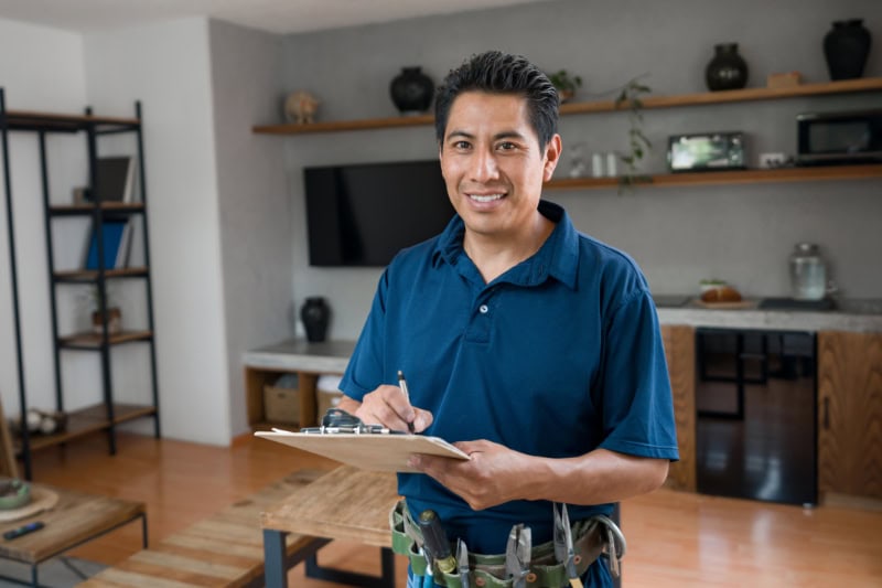 Happy electrician working at a house and looking at the camera smiling while writing on a clipboard.