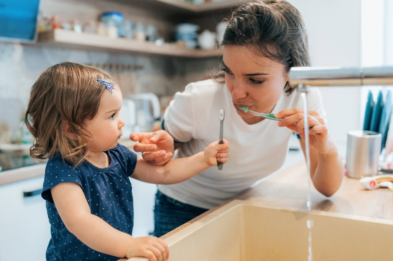 A mom and toddler are brushing their teeth.